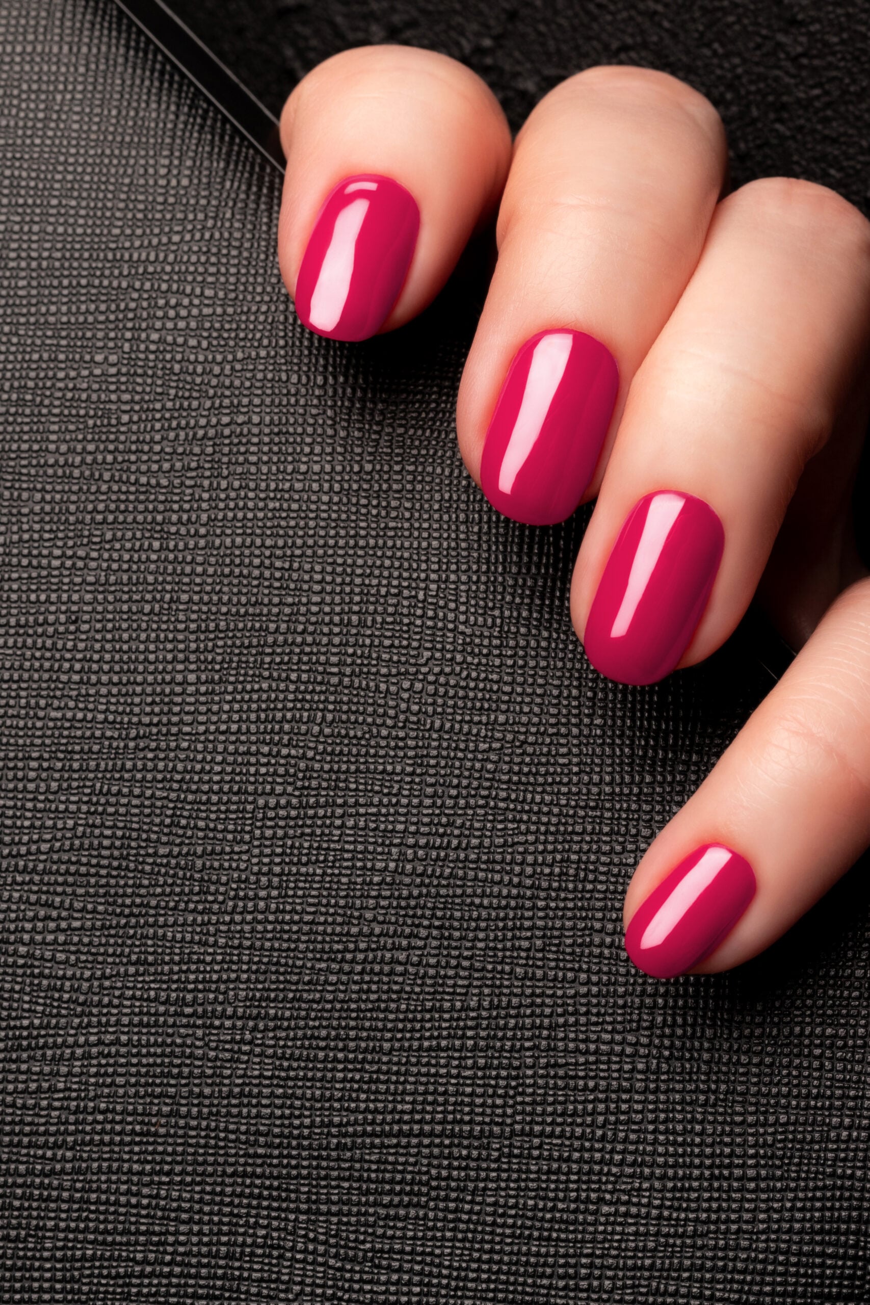 Female hand with beautiful manicure - viva magenta, pink nails on black leather surface background. Nail care concept
